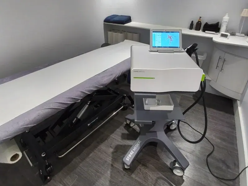 Shockwave therapy (ESWT) equipment beside a treatment bed at PhysioB